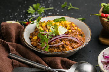 Chili con carne on wooden table with corn and spices