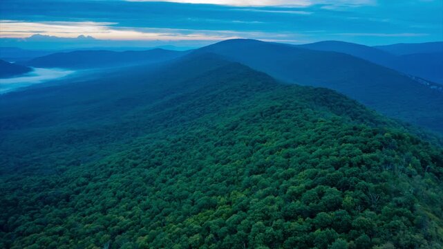 Aerial hyperlapse over Big Schloss and Great North Mountain at dawn, on the border between Virginia and West Virginia, as mist and soft blue light reveal the ridgeline and forested valleys.