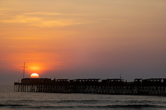 Pier of Pimentel at sunset with birds flying and mast silhouette in Lambayeque, Peru
