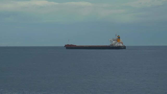 A bulk cargo carrier ship travels on a calm sea, cloudy sky