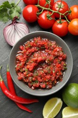 Delicious salsa sauce in bowl and ingredients on dark grey table, flat lay