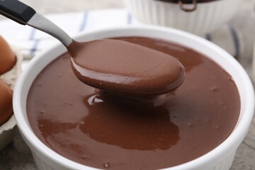 Taking raw chocolate dough from bowl with spoon on grey table, closeup