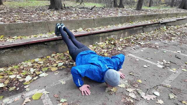 Man doing decline push ups with feet on bench in autumn park, training chest, arms and core strength. Horizontal 4K footage