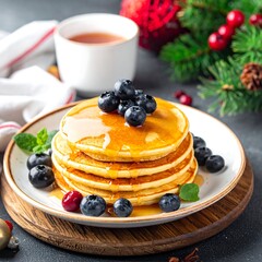 Stack of golden pancakes with syrup, blueberries, tea, and festive decor