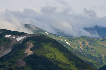 Summer mountain landscape. View of the mountain peaks. Low clouds. Travel, tourism and hiking on the Kamchatka Peninsula. Beautiful nature of Siberia and the Russian Far East. Kamchatka Krai, Russia.