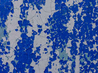 Blue peeling paint on the wall. Old concrete wall with cracked flaking paint. Weathered rough painted surface with patterns of cracks and peeling. Texture for background and design.