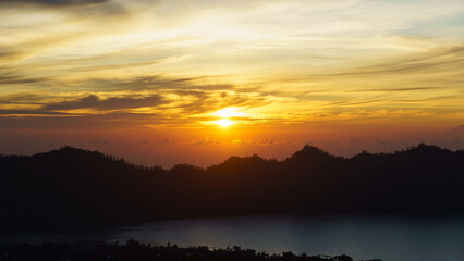 sunset over mountains, golden hour by tranquil lake, sun setting behind mountains with peaceful Kintamani Abang Bali