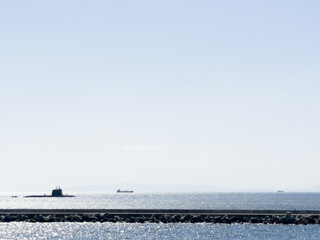 A submarine on the surface of the ocean with sparkling seas and a lighthouse in the foreground