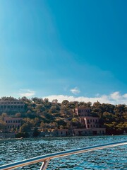 Scenic coastal ruins on a hillside viewed from a boat on turquoise sea, ancient abandoned buildings...