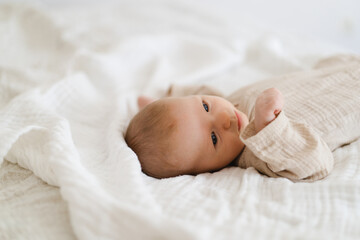 Cute baby lying on a soft white blanket with a calm expression while raising arms. Beautiful portrait of a child. Newborn baby lying on bed