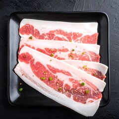Thinly sliced, uncooked pork belly arranged on a black plate