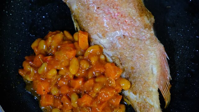 Red sea perch fish with vegetables stew on cooking pan. Cooked with vegetables in samfaina, with tangy tomato caper sauce in a pan. Traditional recipe of Mediterranean gastronomy.