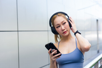 Stretch warm up for sport woman, athletic fit person for outdoor urban workout, wearing headphones smartwatch, holding smartphone choosing music, completing body stretch for exercise readiness