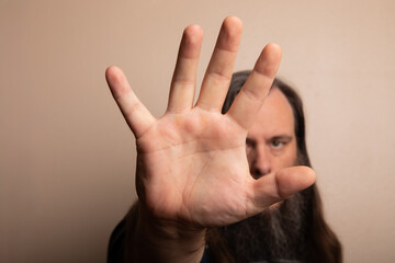A man with a beard and long hair is holding up his hand to block the camera
