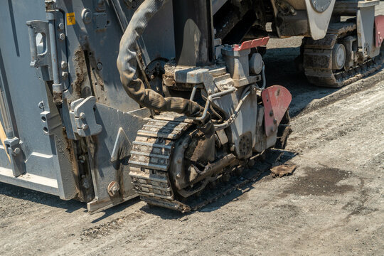 Heavy asphalt milling construction equipment with rotating drum removing worn asphalt layer, preparing road base for new pavement and debris visible, machinery crawler track, moving along work zone