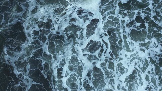 aerial Footage Waves crash against rocks at beach, sea spray in air, sunlight reflects on water at dusk. Natural ocean wave motion