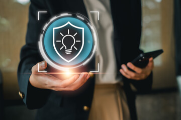 Business professional holding a digital shield with a light bulb, symbolizing intellectual property protection and innovation.
