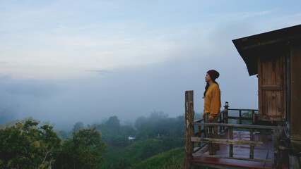 A woman standing on wooden balcony and looking at a mountain views on foggy morning
