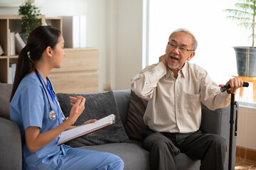 Fototapeta premium Asian Asian elderly man sitting on sofa with walking cane talking with female nurse during home health visit in living room showing concern and warmth
