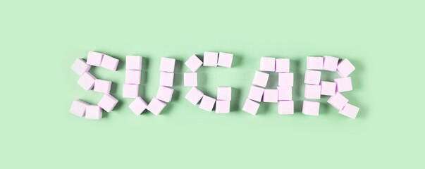 Pink sugar cubes arranged to spell sugar on a soft green background.