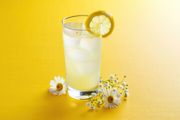 Refreshing tall glass of lemonade with ice and lemon slice garnished with daisies
