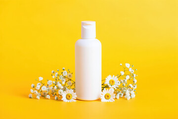White cosmetic bottle surrounded by chamomile flowers on a bright yellow background