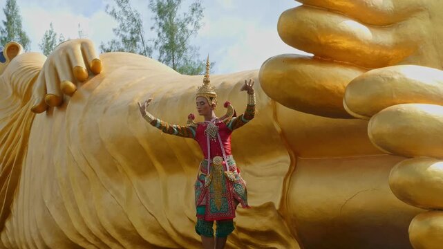A traditional Nora dancer performs gracefully beside the majestic Golden Reclining Buddha, her ornate costume shimmering under soft daylight. The sacred setting reflects Thailand&rsquo;s deep cultural roots