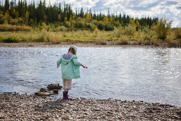 Little girl in mint jacket and boots plays by the river shore.
Sunlight sparkles on calm water surrounded by green forest.
Peaceful outdoor scene captures childhood freedom and nature.
