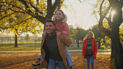 Father giving daughter a piggyback ride in a beautiful autumn park