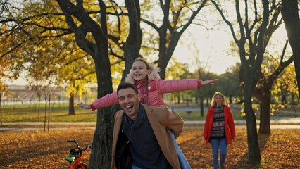 Father giving daughter a piggyback ride in a park during autumn