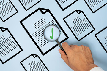Hand holding a magnifying glass over a document with a green check mark. Document verification, quality control, audit, approval, compliance, and inspection concept. © izzuan
