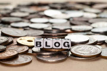 たくさんの硬貨の上に置かれたblogのアルファベットビーズ