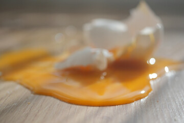 Broken eggshell with spilled yolk on wooden floor 