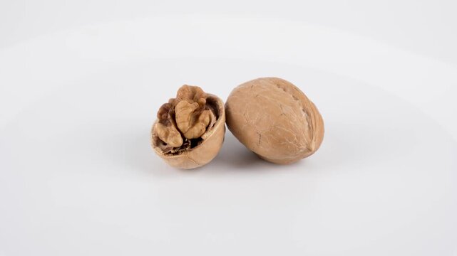 Walnut Close-Up. A single cracked walnut rotates on a white background, showing its detailed texture and kernel inside the shell.