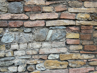A full-frame, detailed texture of a rugged, historic wall constructed from irregular natural stones and a central band of weathered red brick.