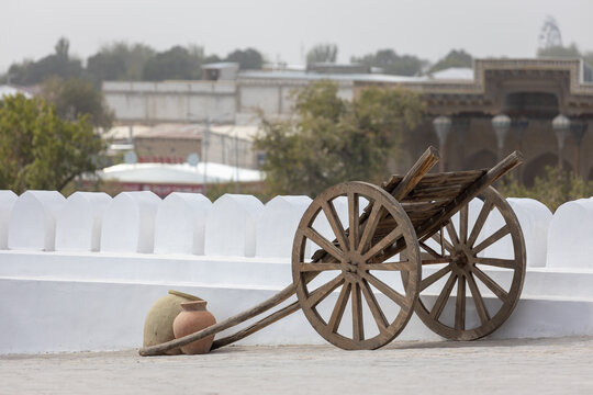 Wooden uzbek araba with clay jugs against white stone wall. Arba is a tall two-wheeled cart or carriage.