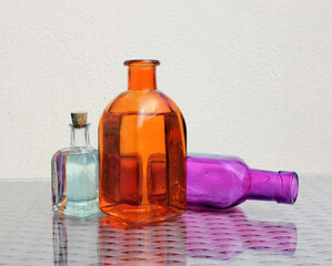 An abstract still life with three small colorful bottles on a glass-topped table. Light background. Selective soft focus.