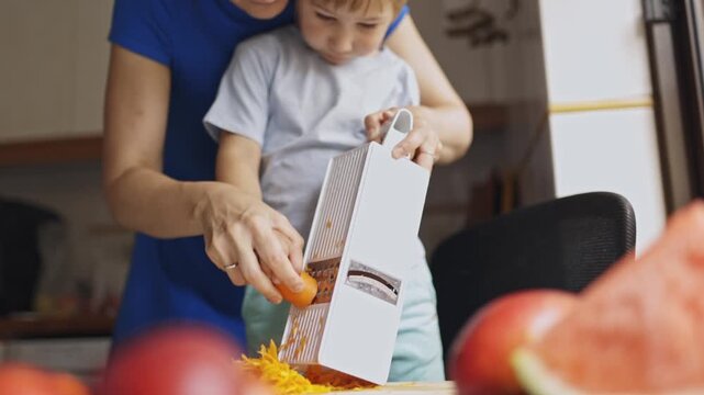 Mother and son grating carrot together in the kitchen