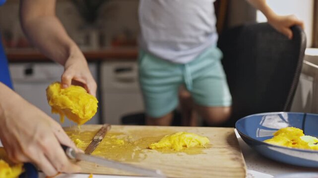 Mother slicing ripe mango for child in kitchen