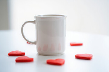 White mug surrounded by red hearts on a white surface