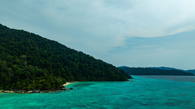 A breathtaking aerial view of a secluded Surin islands with crystal-clear turquoise waters, surrounded by lush green vegetation and corel reef. The pristine white sand and vibrant ocean hues