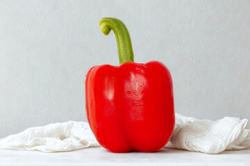 Bright red bell pepper with green stem on white fabric