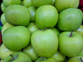 A vibrant close-up of a large, tightly packed pile of crisp, bright green apples