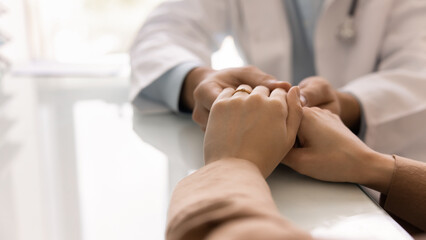 Fototapeta premium Kind doctor holding hands of female patient at medical meeting