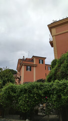 Traditional Orange Italian Building with Balcony Surrounded by Green Garden Under Cloudy Sky