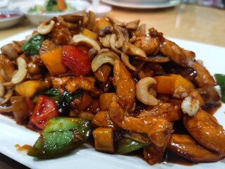 A plate of stir-fried chicken with cashew nuts and colorful vegetables served in a restaurant.