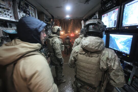 Tactical team operating from a mobile command center at night, monitoring rugged terrain.