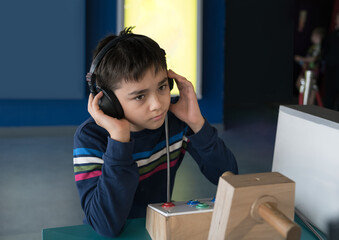 Young boy listening through headphones at science museum exhibit on schol trip. Curious Child learning with interactive educational technology, focused and engaged in auditory experienc