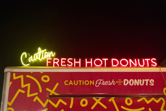 A glowing neon sign reading &ldquo;Caution Fresh Hot Donuts&rdquo; stands out vividly at night above a food truck at the Wairarapa Festival of Christmas, New Zealand.