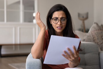 Fototapeta premium Annoyed confused young Hispanic homeowner woman reading paper document